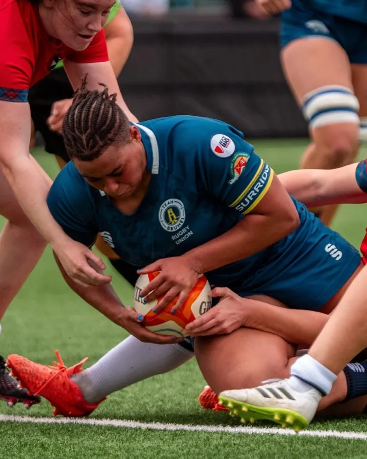 A Brunel women's player in the blue and gold home shirt reaches out to ground the ball over the try line while a defender in red holds on to her.